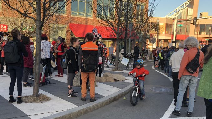A child bikes up a curbside bike lane as people stand along the border, forming a human barrier protecting the bike lane.