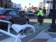 A photo of the Porter Square intersection. In the foreground is a white ghost/memorial bike. In the background, a cyclist wearing a high visibility fluorescent vest is riding in the bike lane, and up ahead a truck is parked in the bike lane,